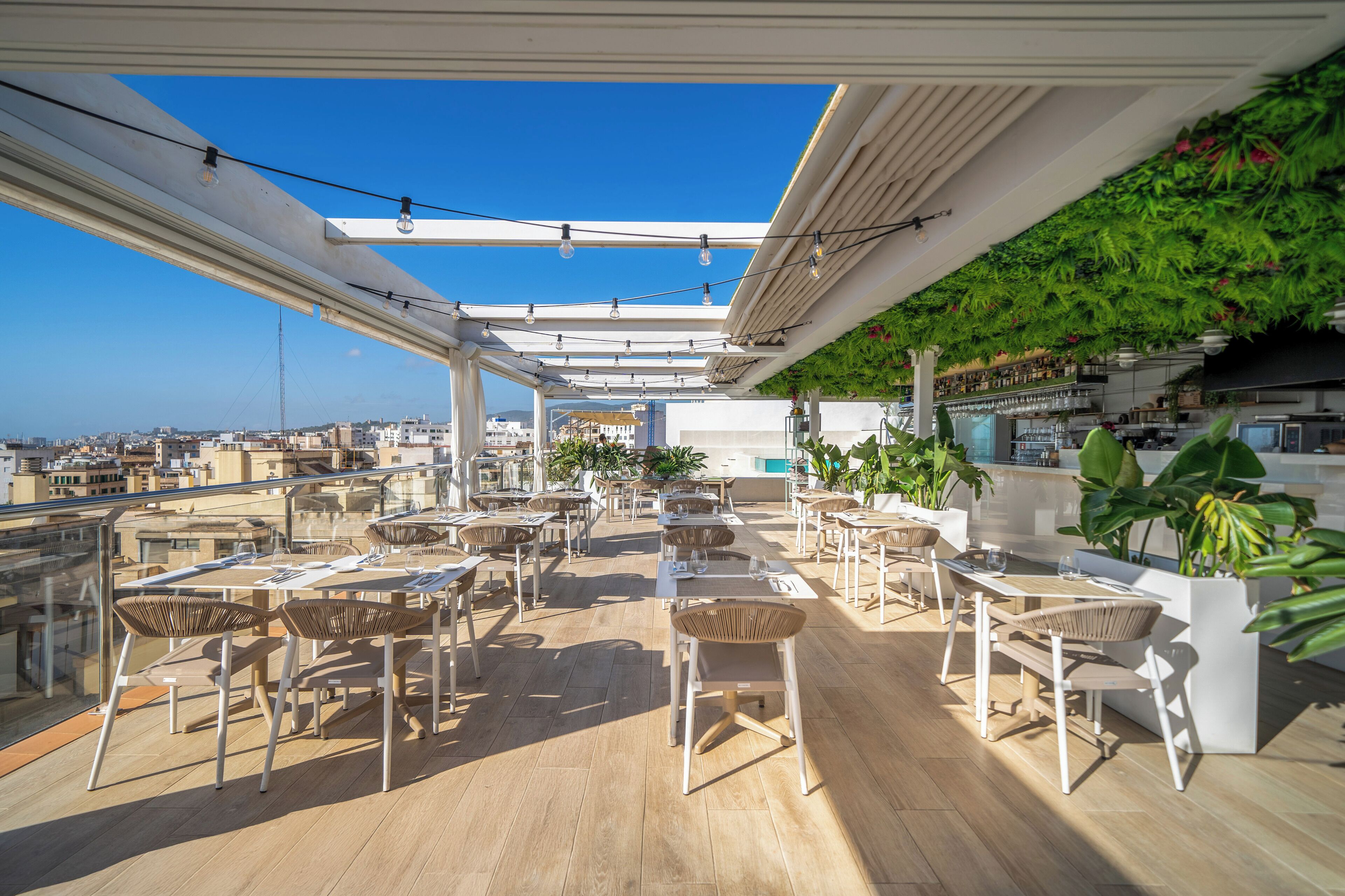 Una terraza al aire libre con mesas y sillas, un área de bar y vistas a la ciudad.