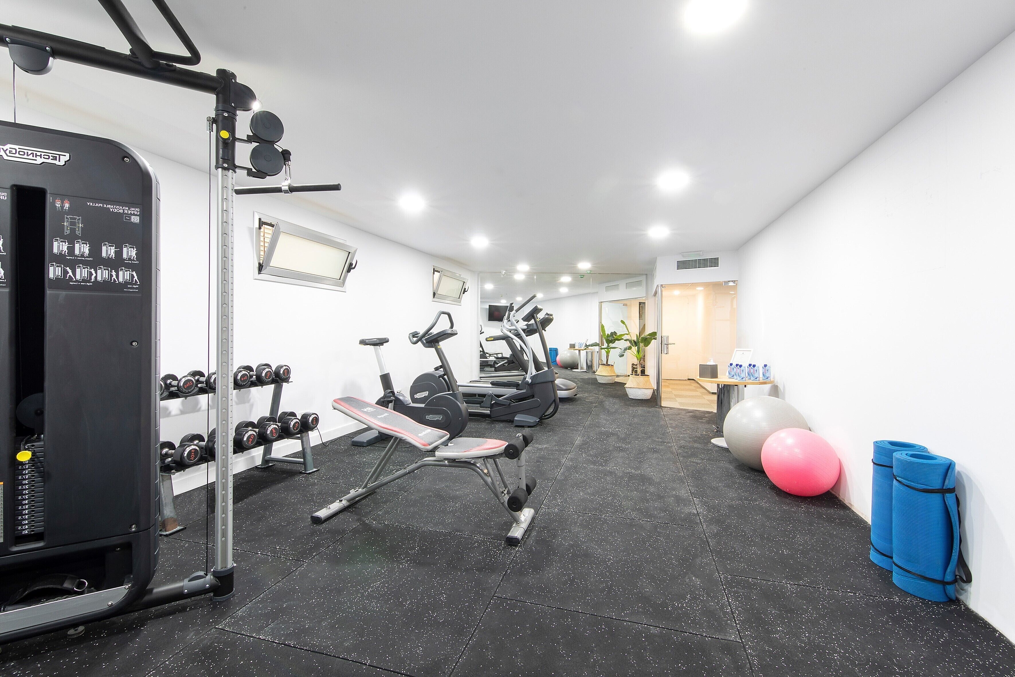 Une salle de sport équipée de divers appareils d’exercice, notamment des haltères, un banc et un tapis de course.