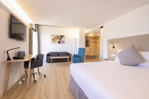 Habitación de hotel con cama, escritorio, silla, sofá y un cuadro en la pared.