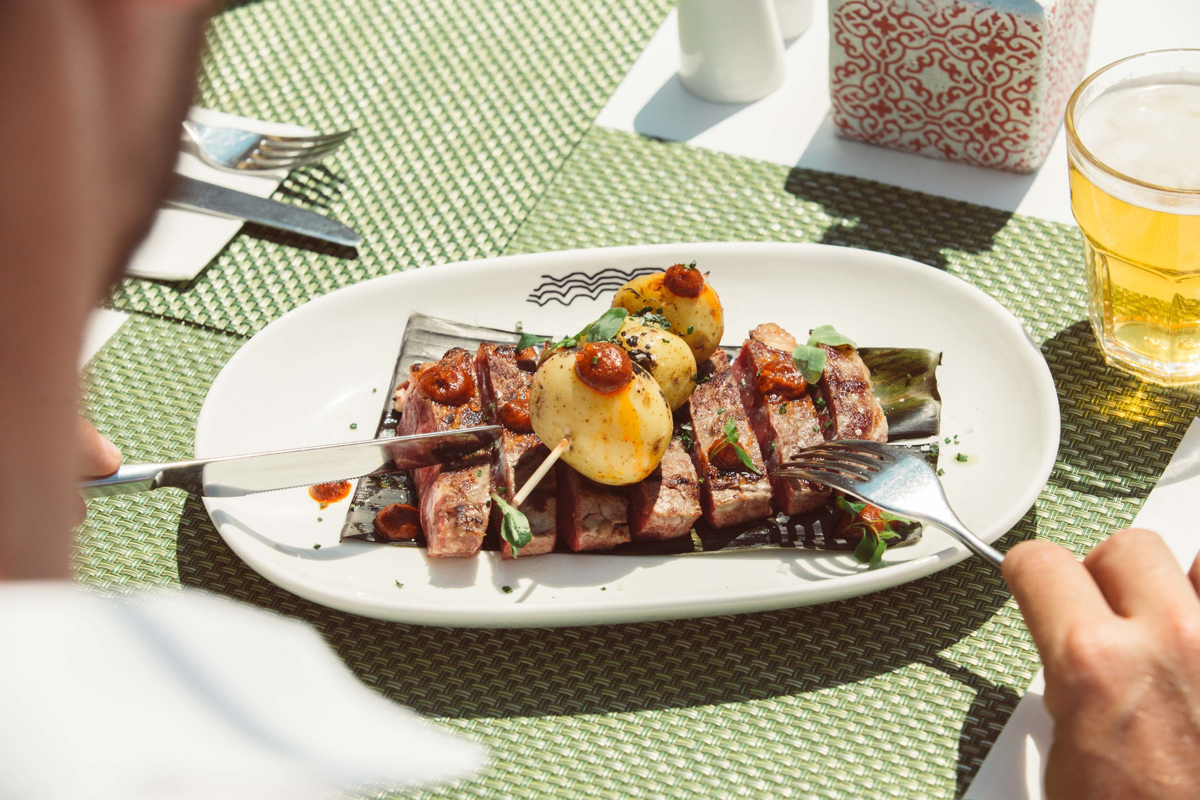 Une assiette de nourriture avec des brochettes, un verre de bière et une nappe à motifs.
