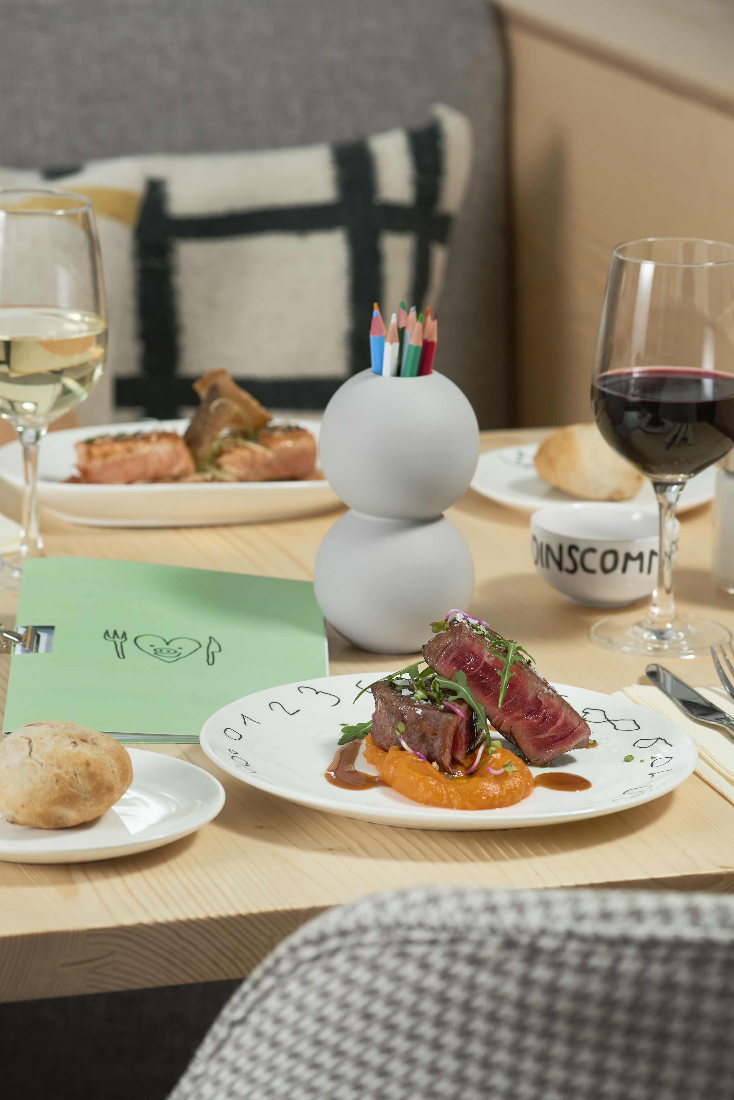 Una mesa de comedor con platos de comida, copas de vino y un bloc de notas con un dibujo.