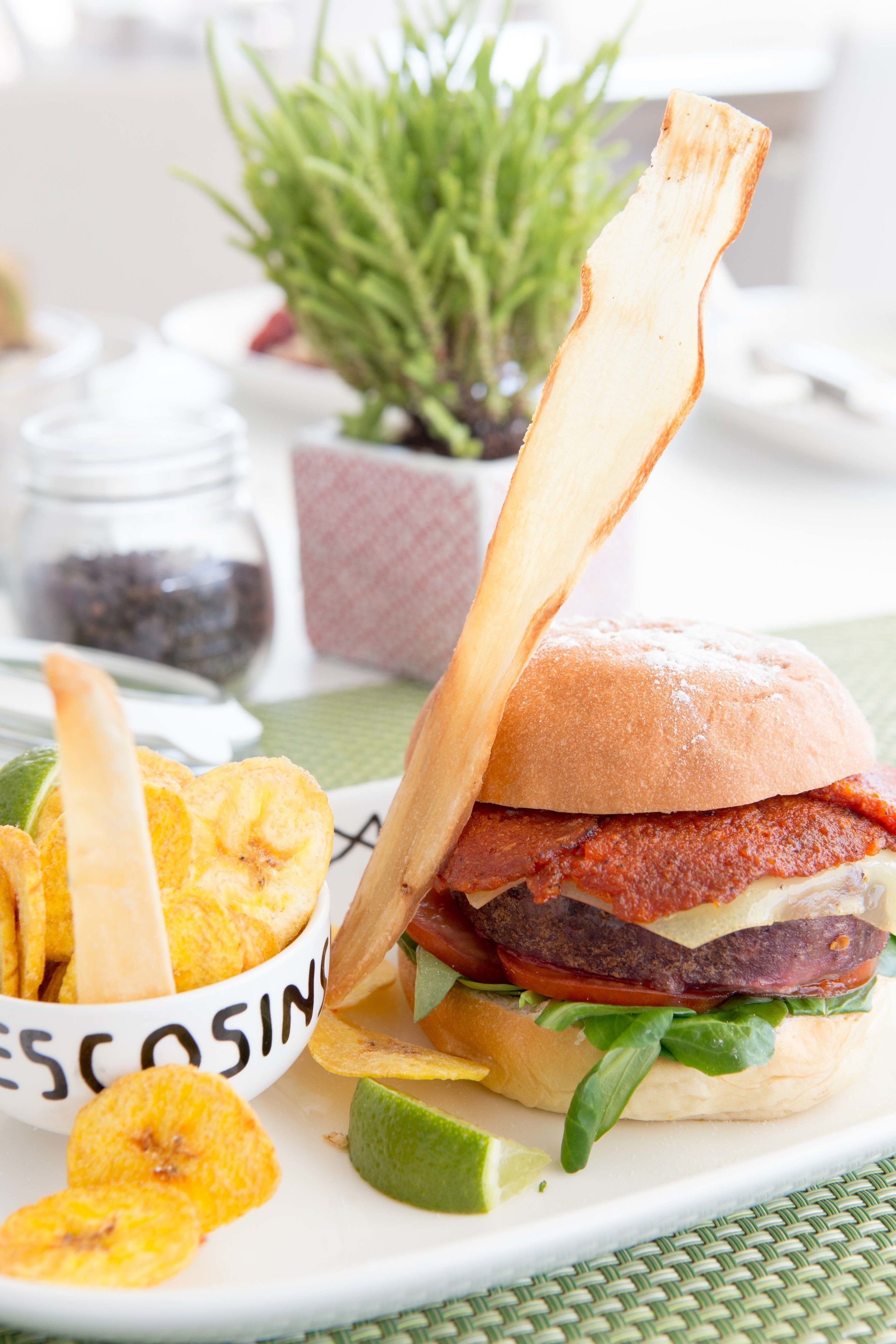 A sandwich with a side of chips and a lime wedge on a white plate.