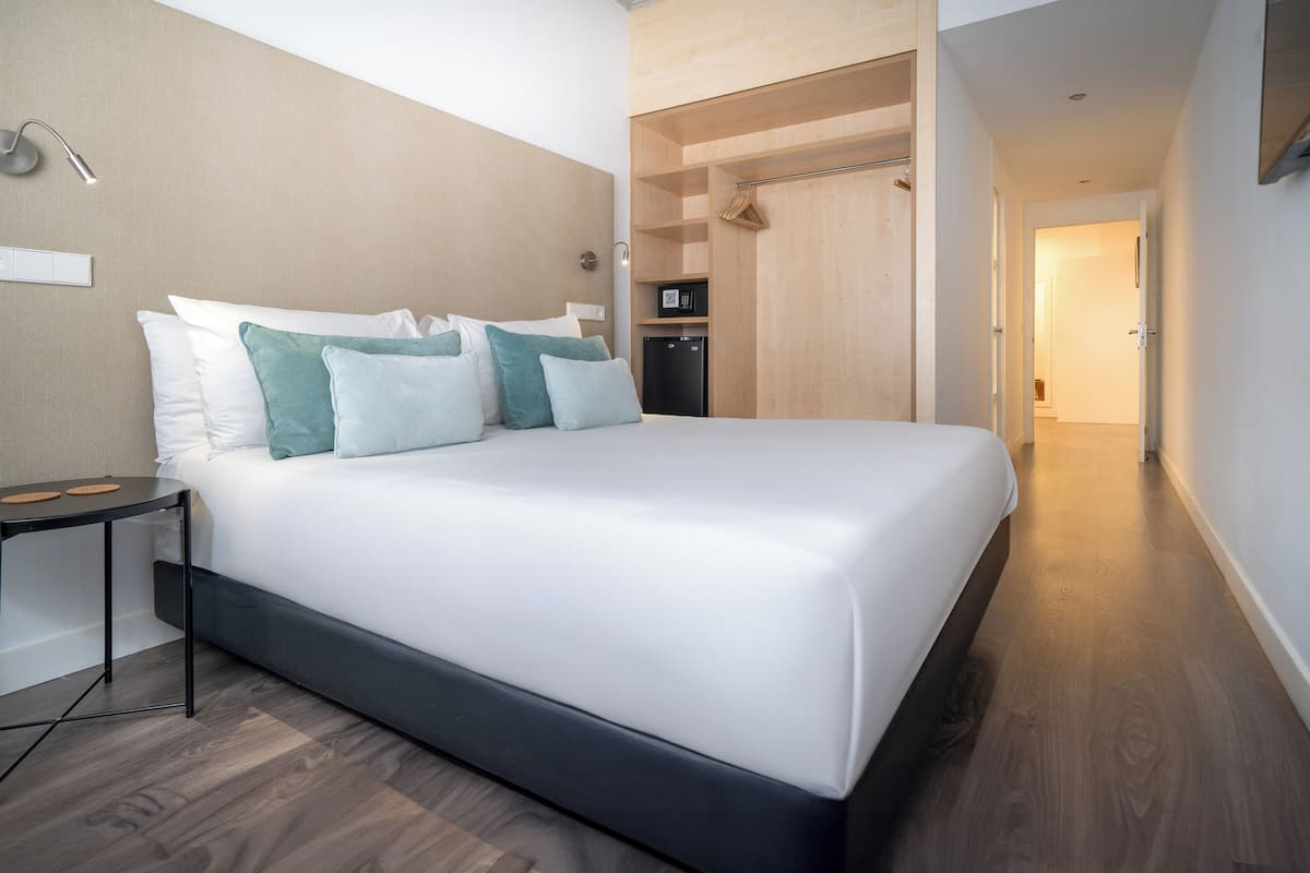Ein modernes Hotelzimmer mit einem großen Bett, einem Nachttisch, einem Kleiderschrank und einem fest installierten Schreibtisch.