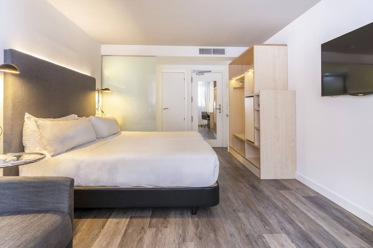 Ein modernes Hotelzimmer mit einem großen Bett, Nachttischlampen, einem Schreibtisch und einem Fernseher.