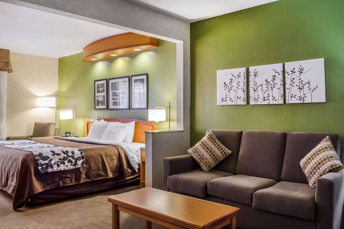 A hotel room with a bed, a sofa, a table, and wall art.