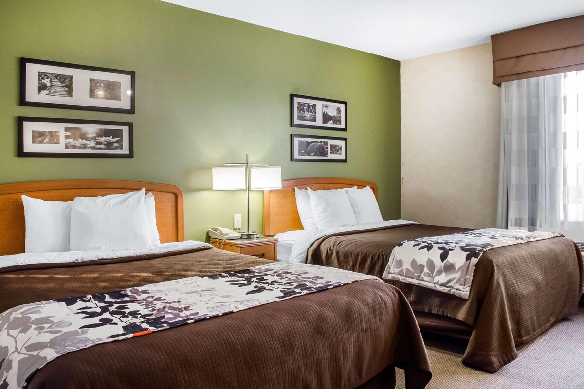 A hotel room with two beds, a nightstand with a lamp, and framed pictures on the wall.