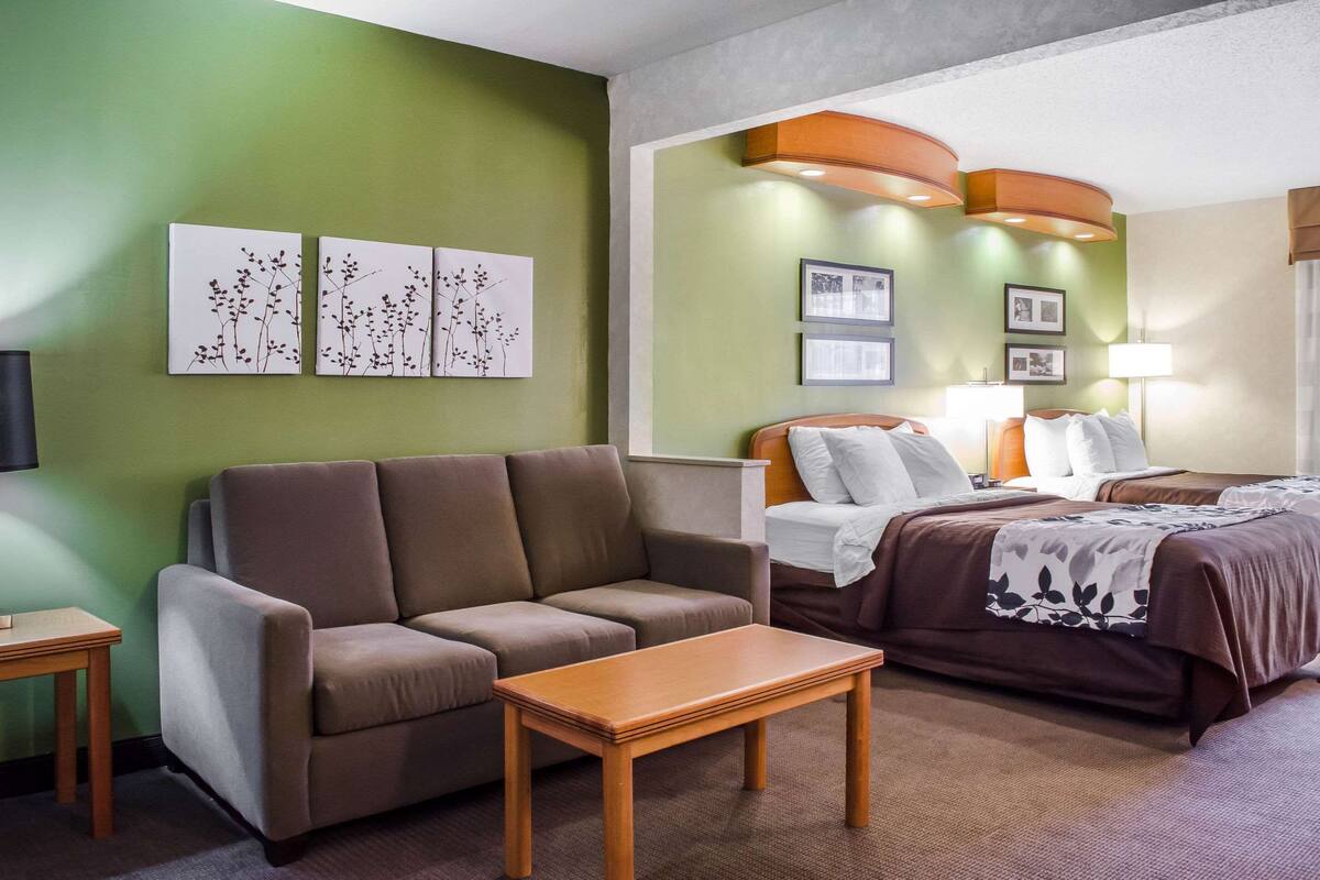 A hotel room with a sofa, a bed with a brown bedspread, a wooden table, and artwork on the walls.