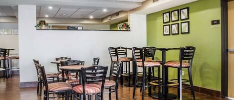 A dining area with multiple tables and chairs, an exit sign, and framed artwork on the wall.