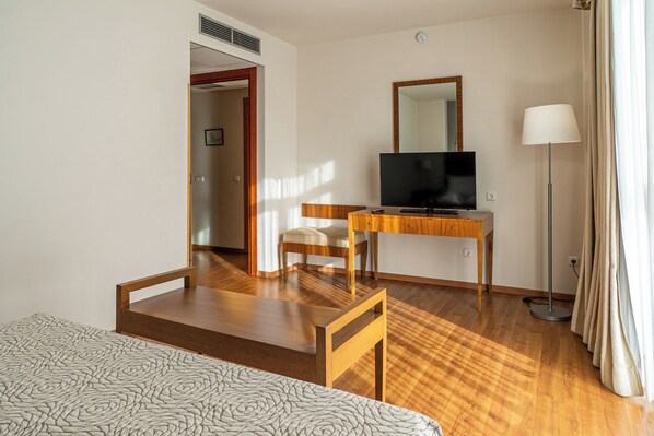 A hotel room with a bed, a desk with a TV, a chair, and a floor lamp.