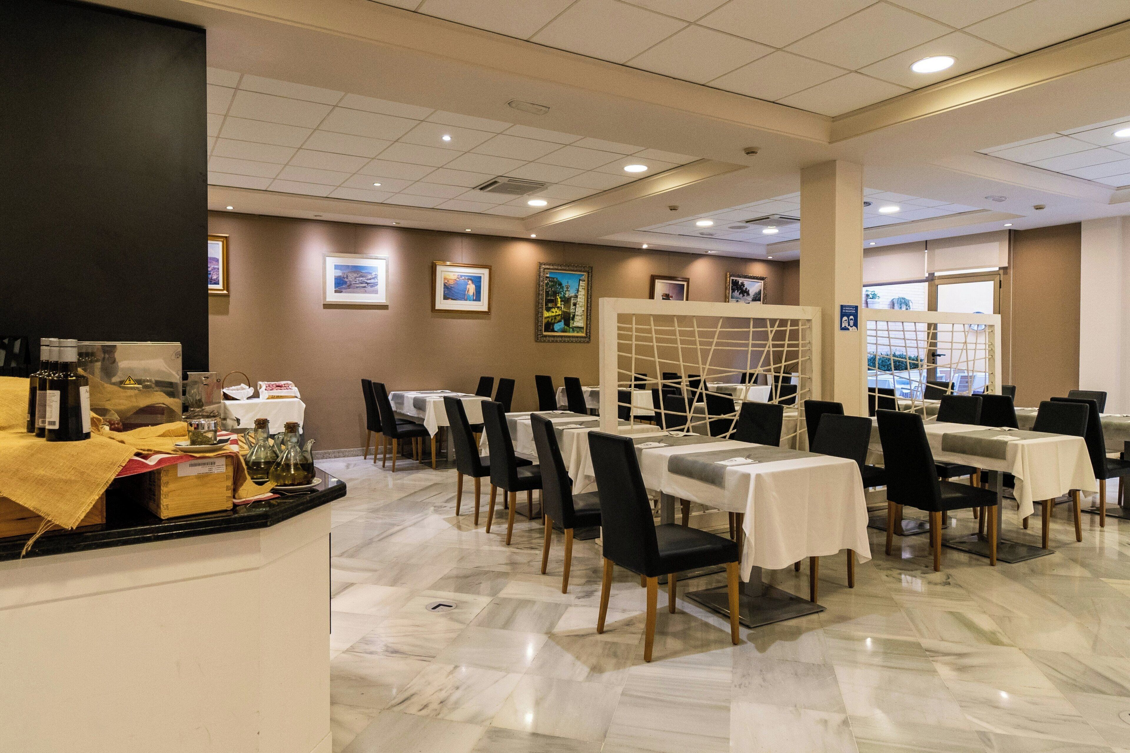 Un restaurante con suelo de mármol, mesas con manteles blancos, sillas negras y cuadros en las paredes.