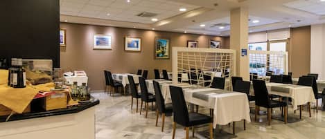 A restaurant with marble flooring, tables with white tablecloths, black chairs, and framed pictures on the walls.