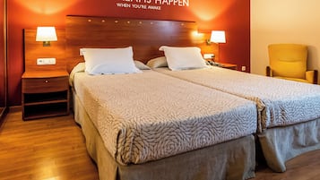 Un lit double avec une couvre-lit à motifs, deux lampes de chevet, une table de chevet, une chaise et un mur orné d’un texte motivant.