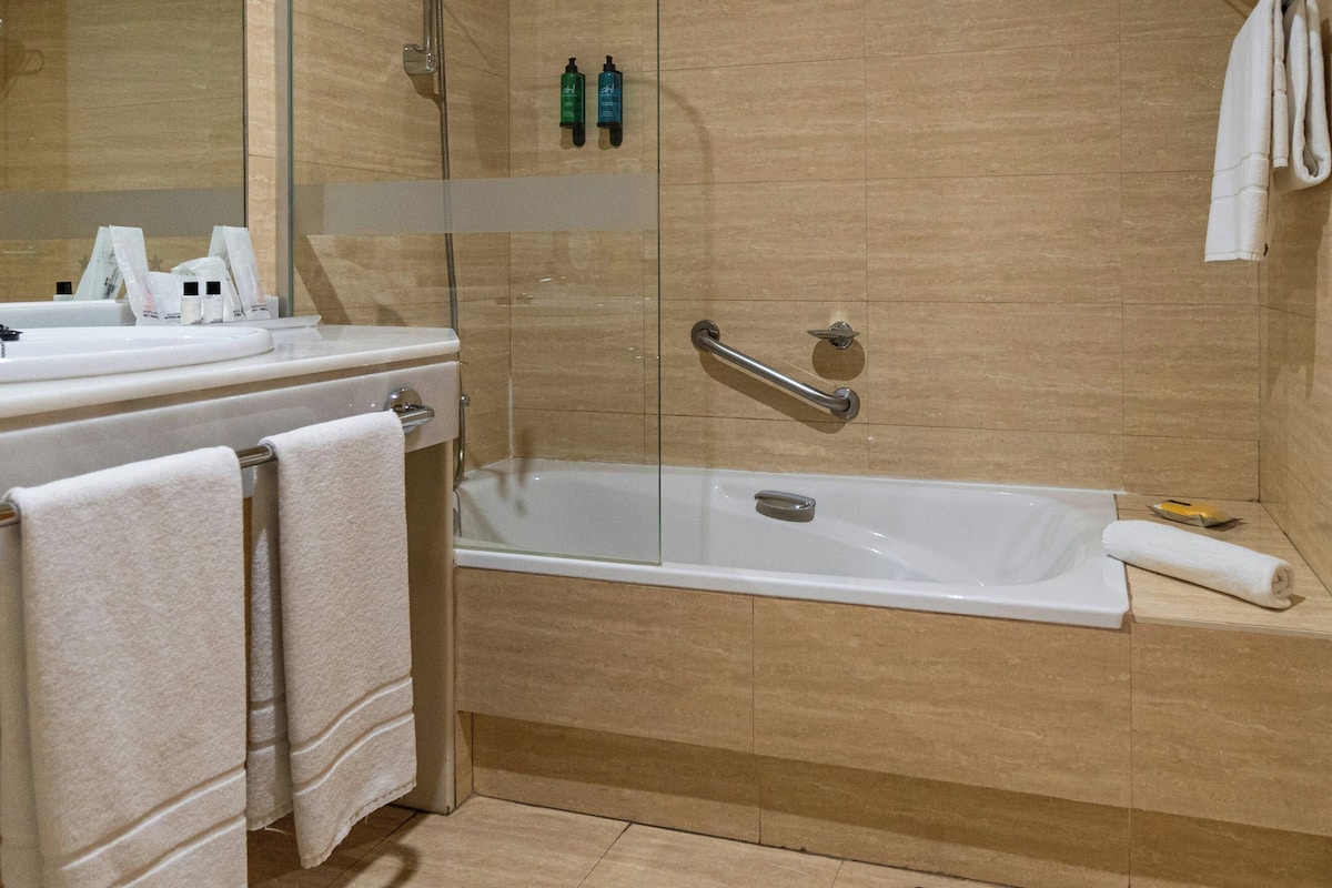 A bathroom with a bathtub, a glass shower enclosure, a vanity with a mirror, and a towel rack.