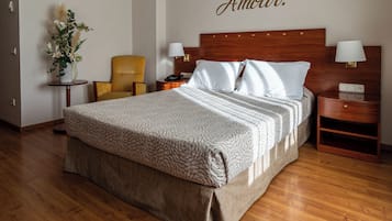 A hotel room with a large bed, a wooden headboard, bedside tables with lamps, a chair, and a decorative wall piece.