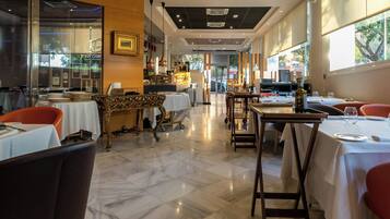 Interior de restaurante com piso de mármore, mesas com toalhas brancas e cadeiras vermelhas.