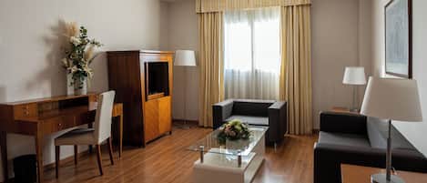 A modern hotel room with a wooden desk, a sofa, a coffee table, and a TV.