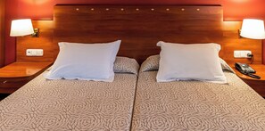 Ein Doppelbett mit einem bettwäschebezug mit Rosenmuster, zwei weiße Kissen, Nachttischlampen, ein Nachttischtelefon und ein hölzernes Kopfende.