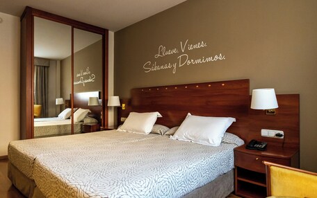 A hotel room with a large bed, a nightstand with a lamp, a mirror, and a wall with a motivational quote.