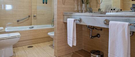 A modern bathroom with a bathtub, toilet, and sink, featuring a mirror, towel rack, and a trash bin.