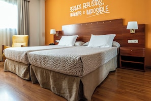 Habitación de hotel con cama doble, dos mesitas de noche con lámparas, una silla y una pared con texto motivacional.