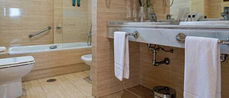 A modern bathroom with a bathtub, toilet, and sink, equipped with a towel rack and a trash bin.