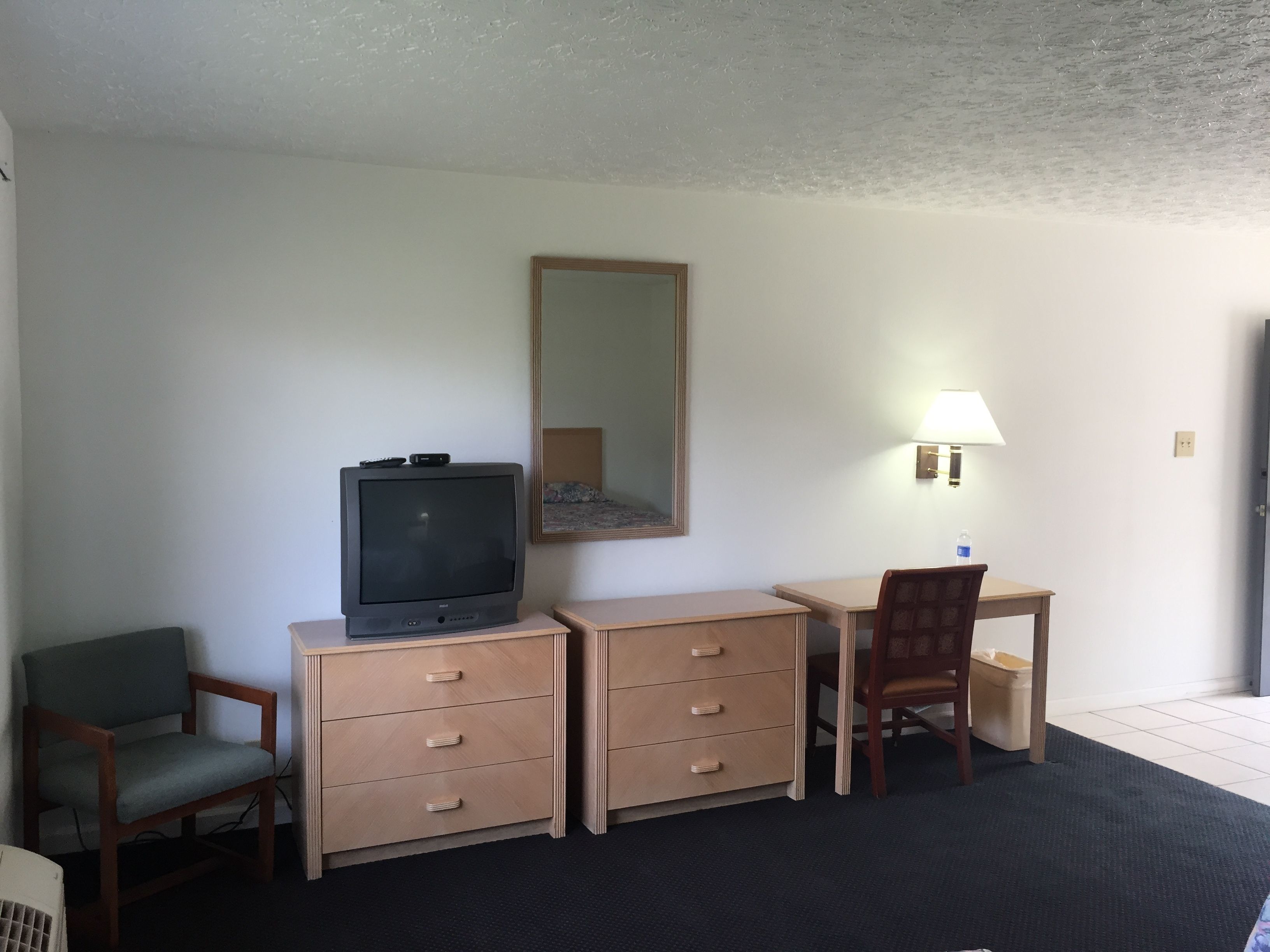 A compact hotel room with a single bed, a desk with a chair, a television, a dresser, and a mirror.