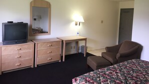 Ein Hotelzimmer mit einem Bett, einem Fernseher auf einer Holzkommode, einem Schreibtisch mit Lampe und einem Stuhl.