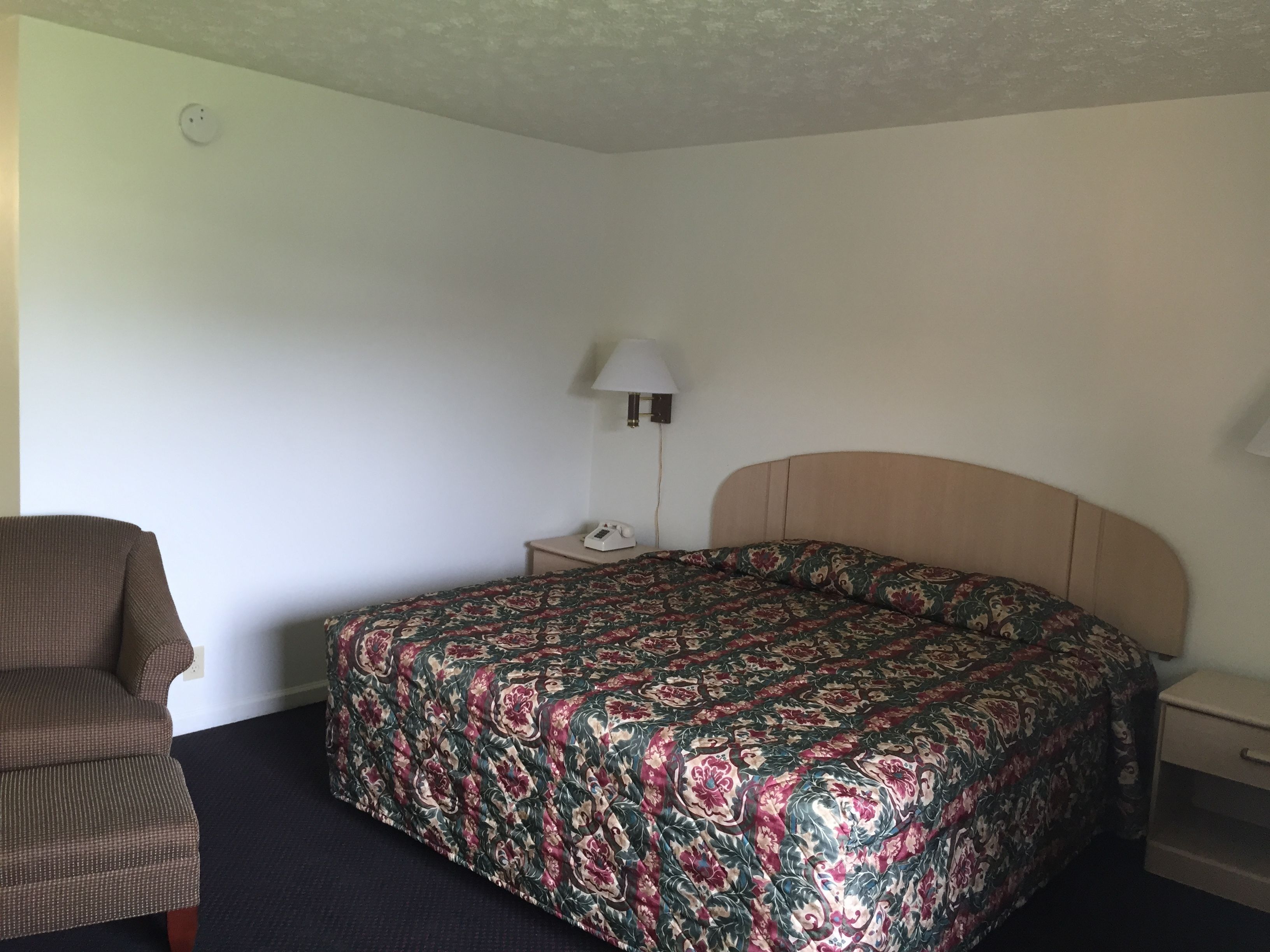 Ein Hotelzimmer mit einem Einzelbett, einem Sessel, einem Nachttisch und einer Lampe.