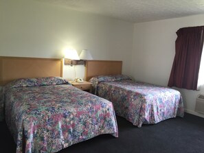 A hotel room with two beds, a nightstand with a lamp, and a window with curtains.