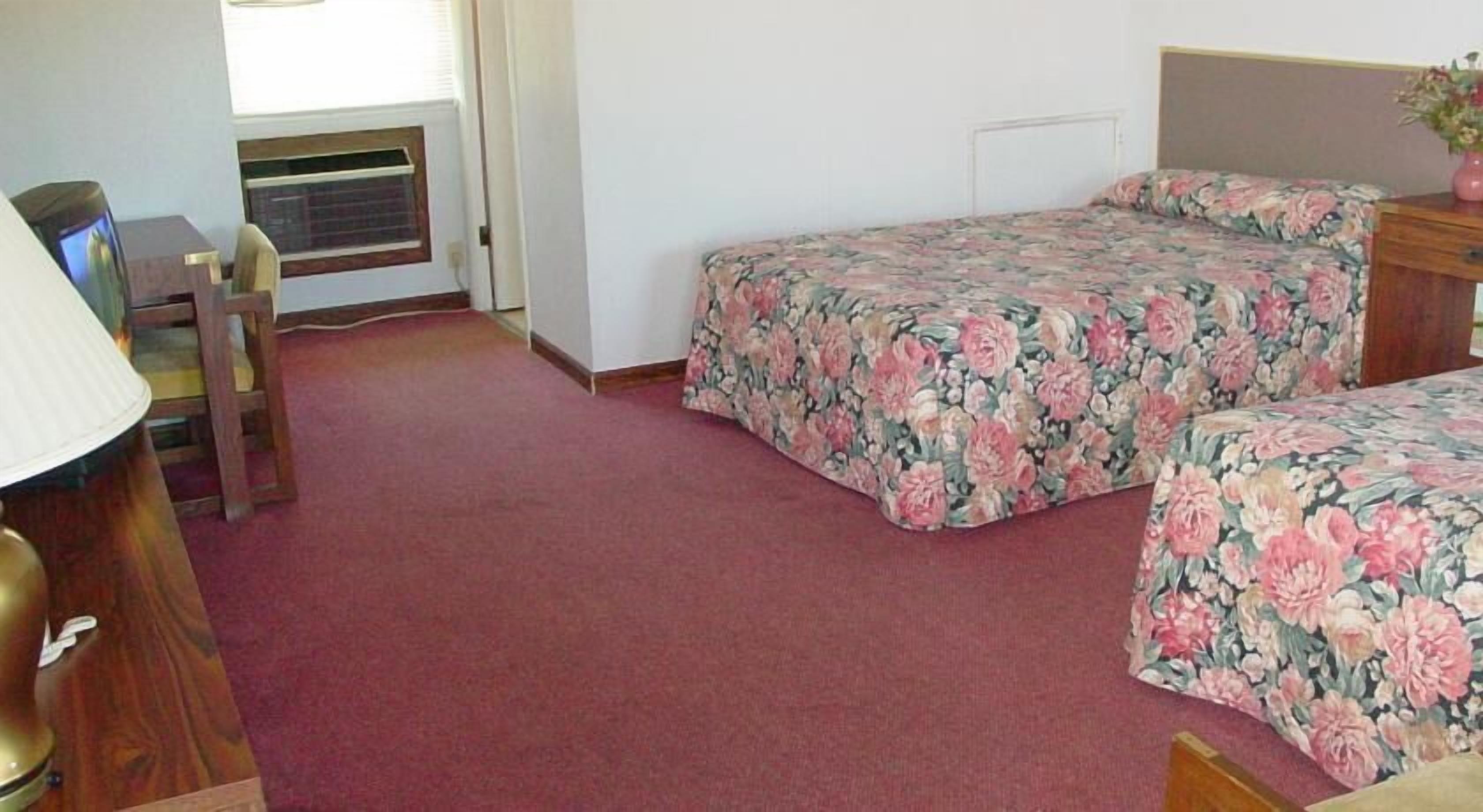 A room with two beds, a desk, a chair, and a radiator.