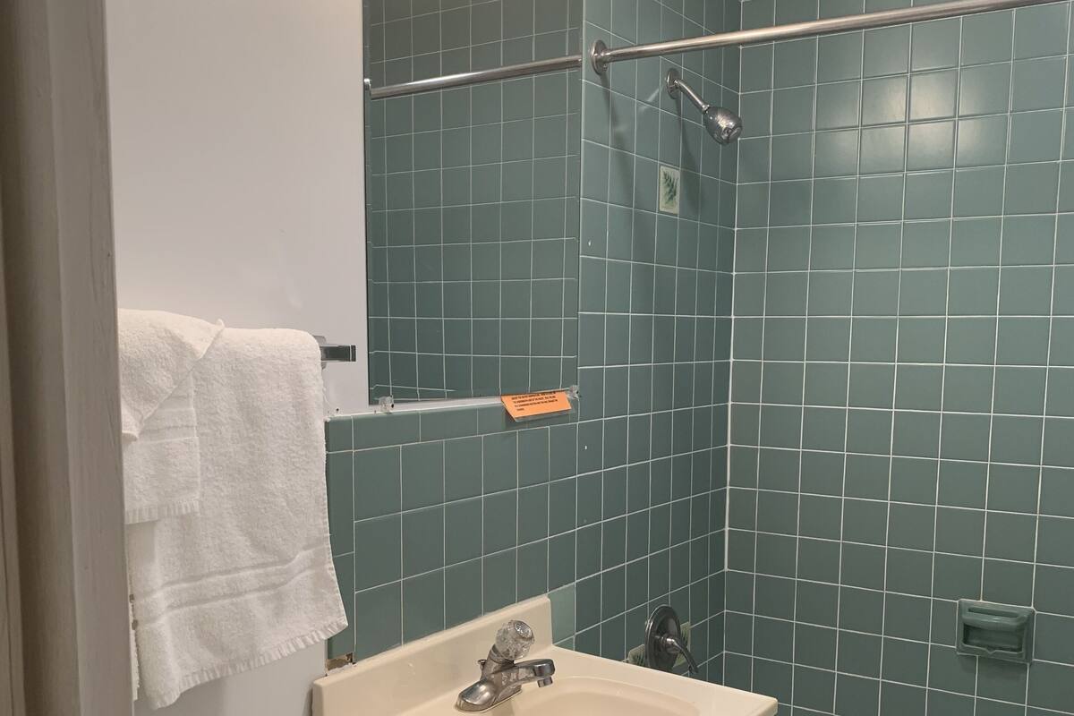 A bathroom with a white sink, a mirror, a towel rack, a shower, and a green tiled wall.