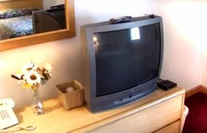 Un televisore su una cassettiera di legno, con un vaso di fiori e un telefono.
