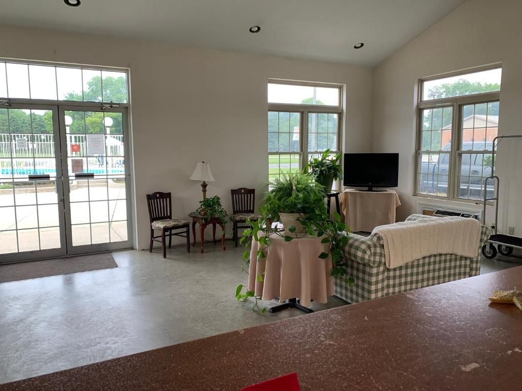 Quarto espaçoso com grandes janelas, televisão, mesa com planta e cadeira de rodas.