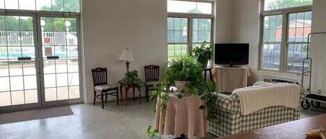 A spacious room with large windows, a television, a table with a plant, and a wheelchair.
