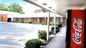 A motel with a Coca-Cola sign, a covered parking area, and a building with a flat roof.