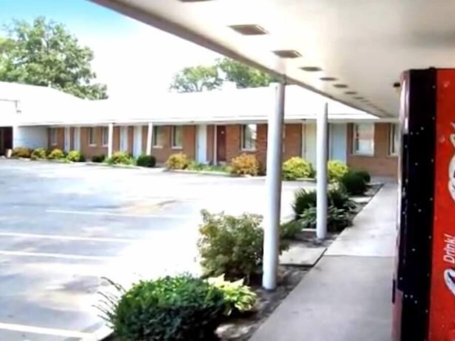 A motel with a Coca-Cola sign, a covered parking area, and a building with a flat roof.