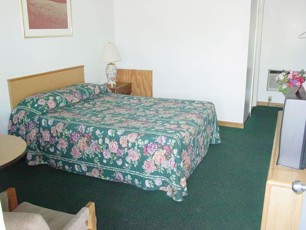 A standard hotel room with a bed, a bedside table with a lamp, a small round table, and a dresser.
