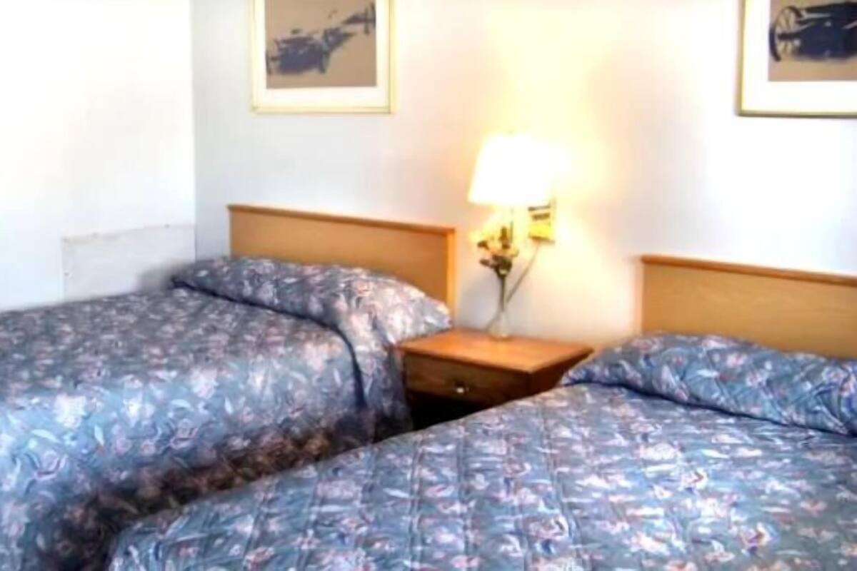 A hotel room with two beds, a nightstand, and a wall-mounted lamp.