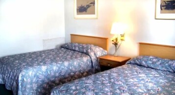 A hotel room with two beds, a nightstand, and a wall-mounted lamp.