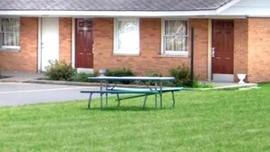 A motel with two doors, a parking lot, and a picnic table in the front yard.