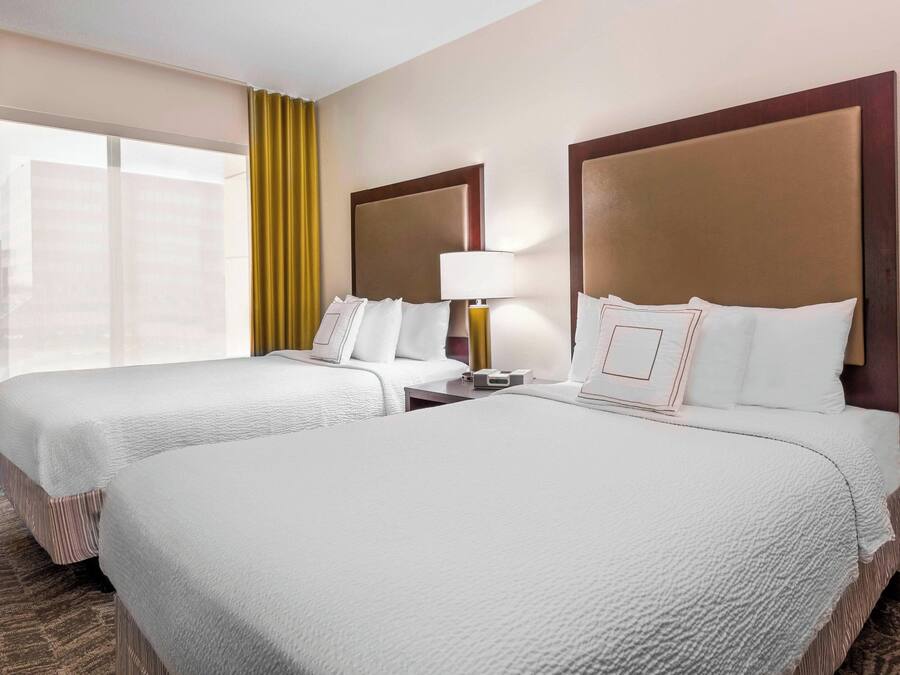 A hotel room with two beds, a nightstand, a lamp, and a window with curtains.