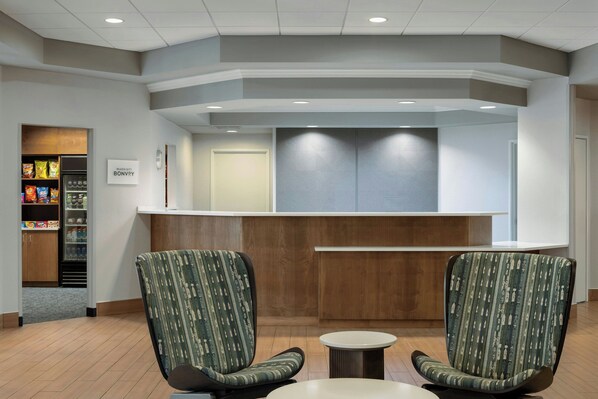 A reception area with two upholstered chairs, a small round table, a vending machine, and a reception desk.