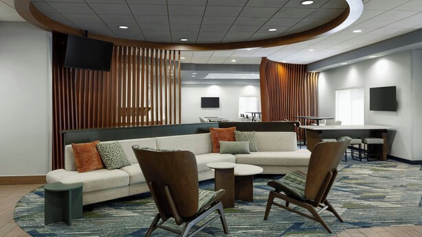 A modern hotel lobby with a sectional sofa, two armchairs, a small coffee table, a TV mounted on the wall, and a bar area with stools. - SpringHill Suites by Marriott Frankenmuth (Frankenmuth)