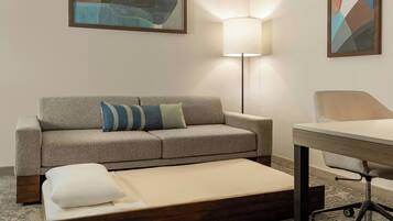 A hotel room with a sofa, a small table, a lamp, and a bed.