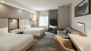 Une chambre d’hôtel avec deux lits, un bureau, une chaise, une télévision et un tableau au mur.