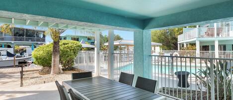 A covered outdoor area with a pool, a table with chairs, and a view of the pool area.