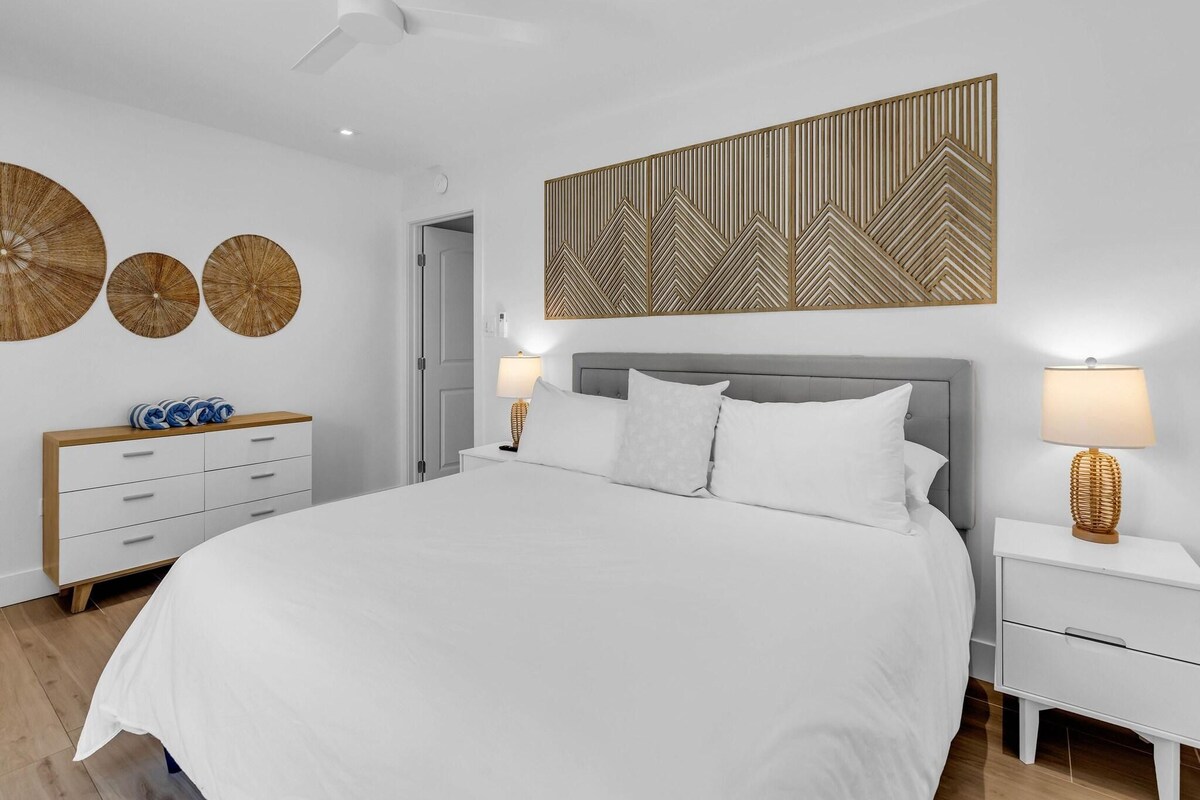 A modern bedroom with a large bed, two bedside tables, a ceiling fan, and decorative wall art.