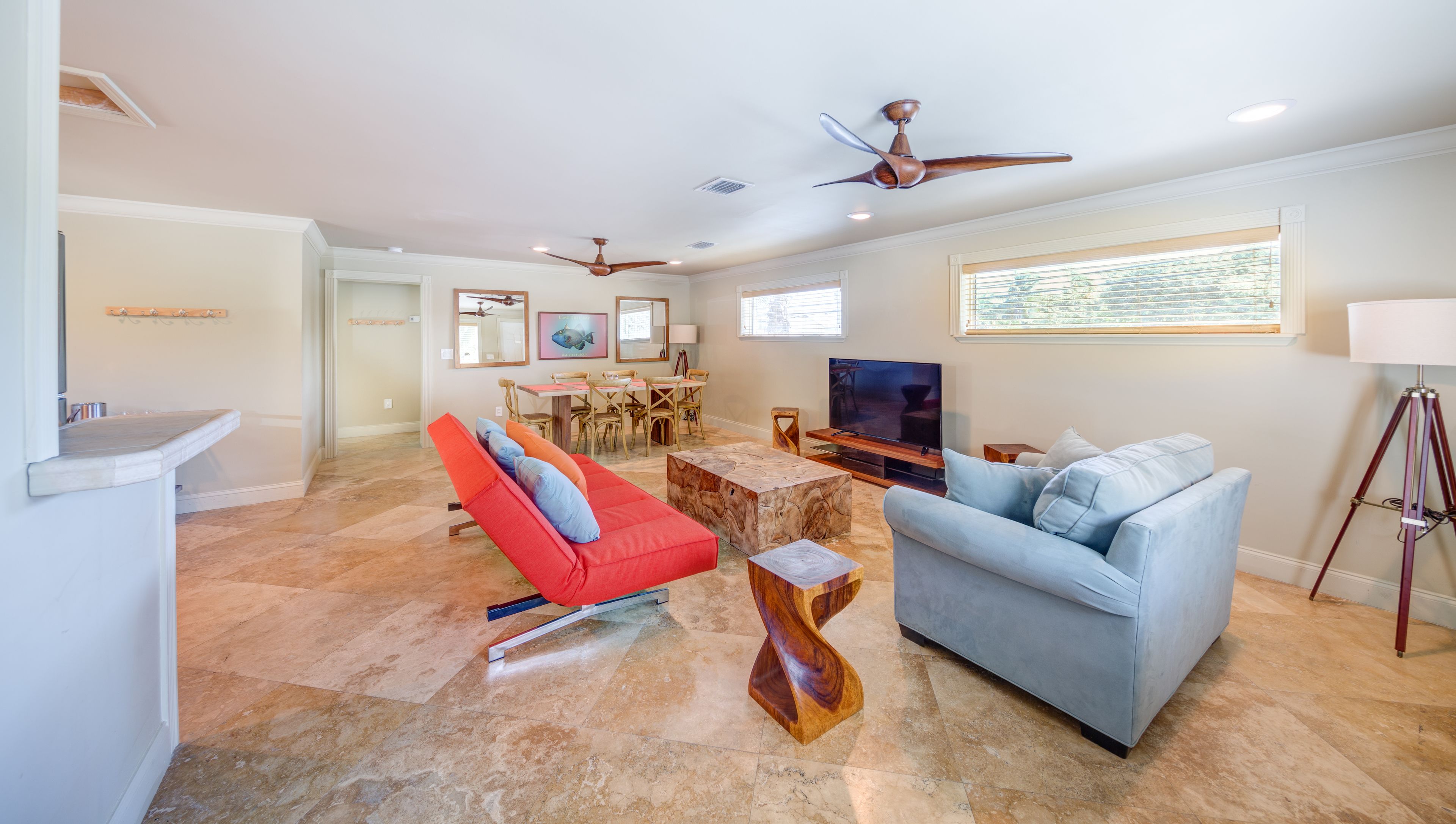 A spacious living room with a red chair, a blue sofa, a wooden coffee table, and a TV.