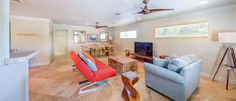 A spacious living room with a red chair, a blue sofa, a wooden coffee table, and a TV.
