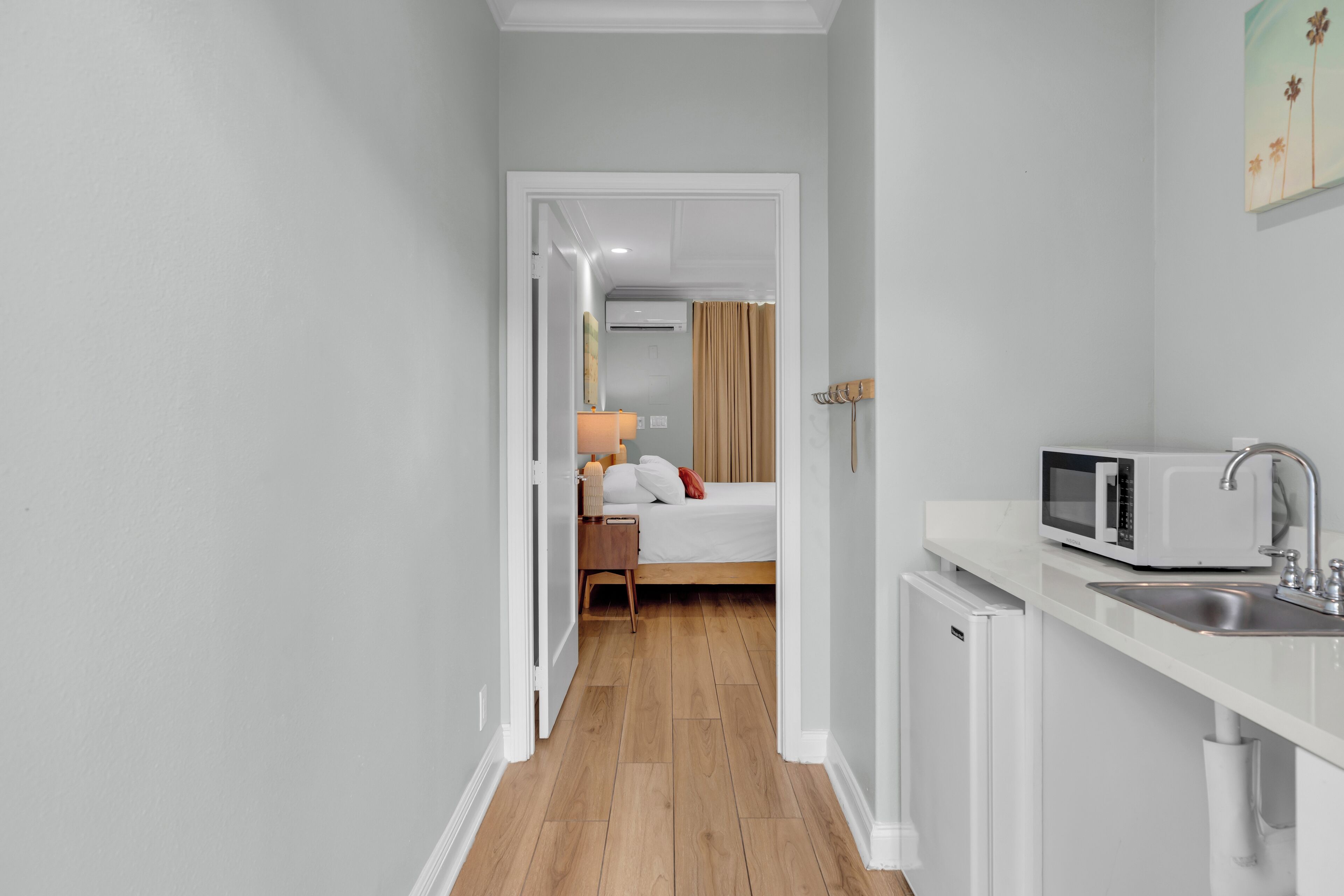 Camera d'albergo compatta con angolo cottura, un letto e un bagno visibile attraverso una porta aperta.
